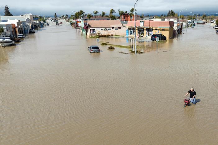 An aerial view shows a man navigating floodwaters with his bicycle in the unincorporated community of Pajaro in California on March 11. Residents were forced to evacuate in the middle of the night after an atmospheric river surge broke the Pajaro Levee and sent flood waters flowing into the community.