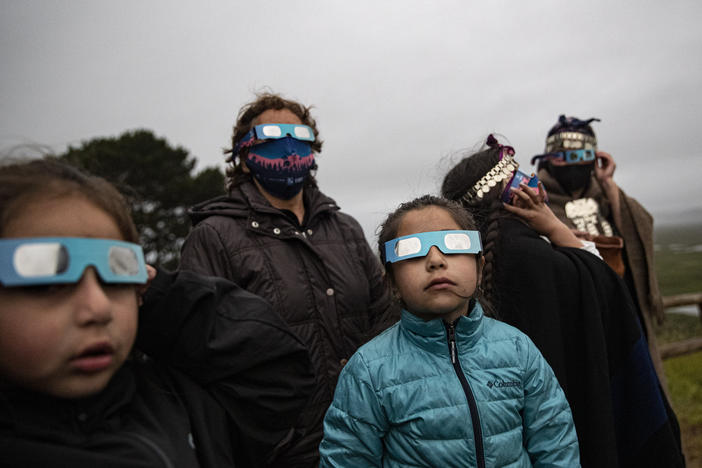A Mapuche Indigenous family uses special glasses to try and observe a total solar eclipse in Carahue, La Araucania, Chile, Monday, Dec. 14, 2020. The total eclipse was barely visible from Carahue because of an overcast sky.