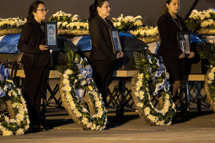 Foreign Ministry officers hold portraits beside the coffins of Guatemalan migrants whose remains arrived at the La Aurora Air Force Base in Guatemala City on Tuesday. The Mexican Air Force transported the bodies of 17 migrants who died in a fire at an immigration detention center in Ciudad Juárez, Mexico.
