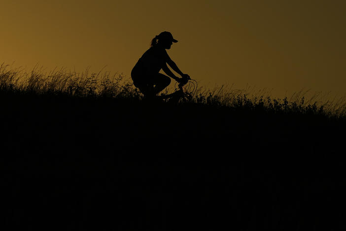 A cyclist passes through a park during an evening ride, Monday, June 26, 2023, in San Antonio.