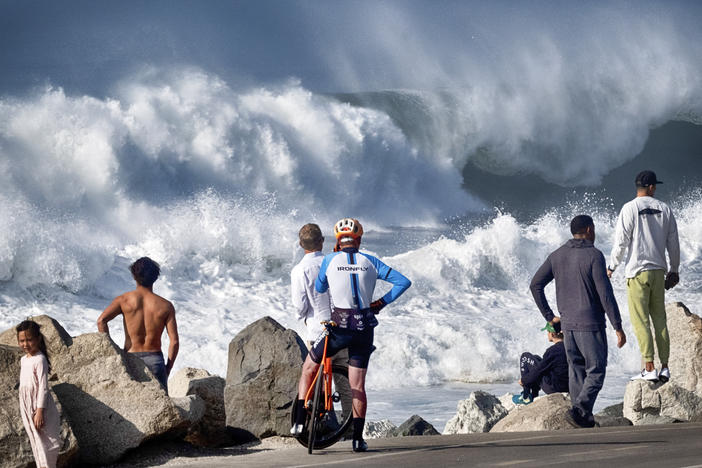 Beachgoers watch as turbulent surf pounds the coast on Thursday in Manhattan Beach, Calif.