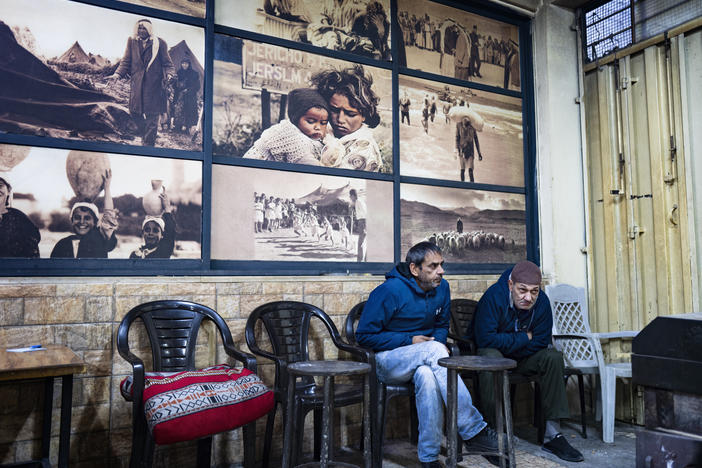 Inside a cafe in the Al Ama'ari refugee camp in the occupied West Bank, men huddle around a wooden stove for warmth in front of a large mural of photographs from 1948, when many Palestinians were forcibly displaced from their homes.