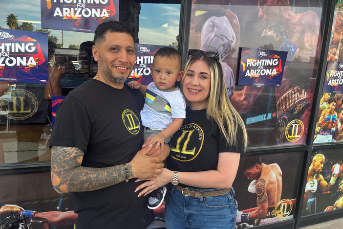 Junior Lopez, owner of JL Boxing Academy in Phoenix, stands outside his business with his wife, Mayrelis Gomez, and their young son.
