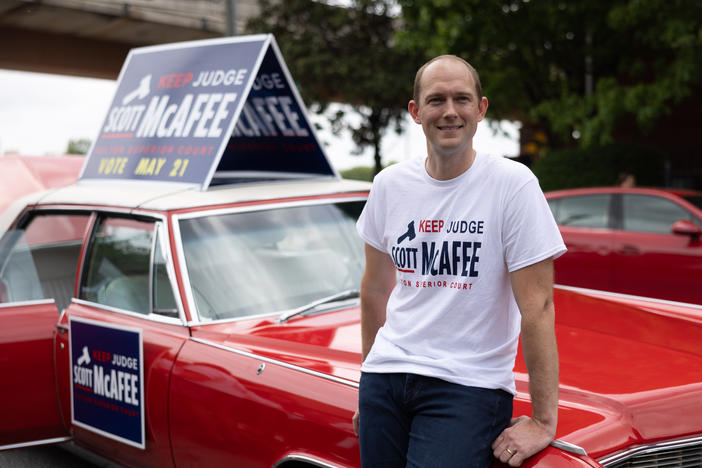Fulton Superior Court Judge Scott McAfee leans against a 1965 Cadillac Fleetwood that has been in his family for years, while campaigning at a parade in Atlanta on April 27. McAfee, the trial judge in the Georgia election interference case, is up for reelection this month in a nonpartisan race.