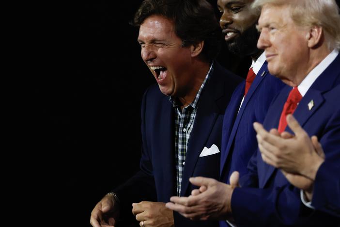 Right-wing personality Tucker Carlson laughs as he stands alongside Congressman Byron Donalds, Republican presidential candidate Donald Trump, and vice presidential candidate J.D. Vance on the first day of the Republican National Convention in Milwaukee.