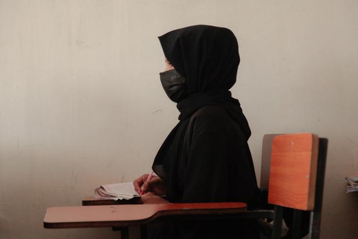 A teenage girl wearing a face mask, head scarf and long black robe, listens to a math teacher at a tutoring center in Kabul. The center was established by a women's rights activist to circumvent a Taliban ban on girls attending secondary school. The activist said she has informal permission by Taliban authorities to run the center as long as teenage girls abide by a strict dress code.