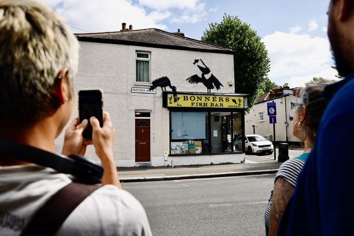 People gather to look at an artwork by street artist Banksy depicting two pelicans catching fish, painted on top of a fish-and-chips shop in Walthamstow, northeast London, on Aug. 9.