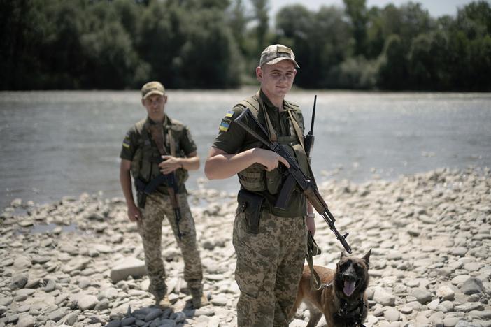 Ukrainian border guards pose with their dog on a pebble beach on the Tisza River bordering Romania, in Velykyi Bychkiv, Ukraine, on July 10.