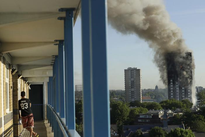 A resident in a nearby building watches smoke rise from the Grenfell Tower building on fire in London on June 14, 2017. 