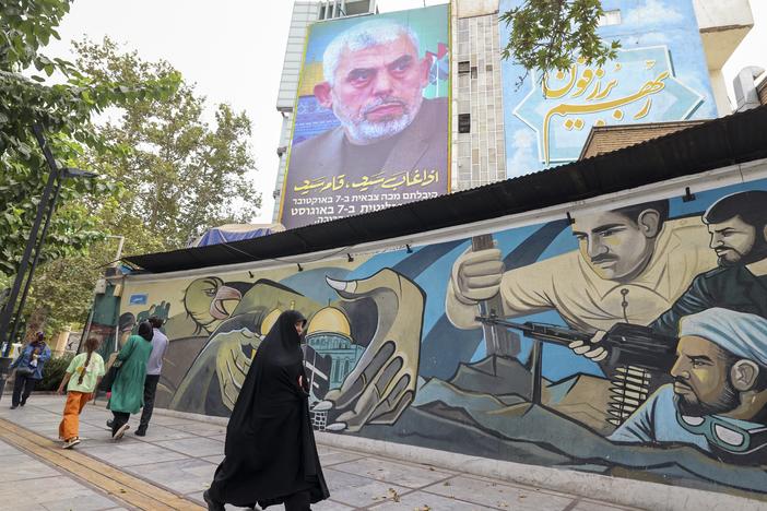 People walk past a billboard showing a portrait of Hamas leader Yahya Sinwar (top) next to Palestine Square in the Tehran on Aug. 12, 2024.