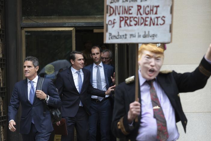 Attorneys for former President Donald Trump, John Lauro (left) and Todd Blanche (second left), depart the E. Barrett Prettyman U.S. Courthouse in Washington, D.C., in 2023, near a protester wearing a costume in Trump's likeness.