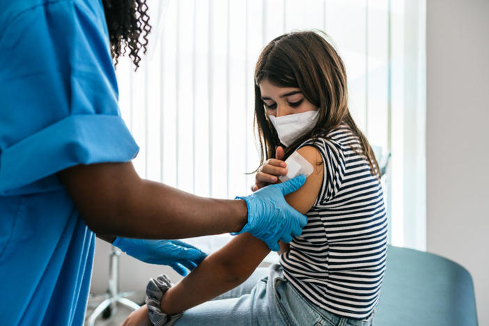 Unrecognizable female doctor or nurse putting a bandage after Covid-19 vaccination at vaccination center. Caucasian preteen girl in vaccination center.