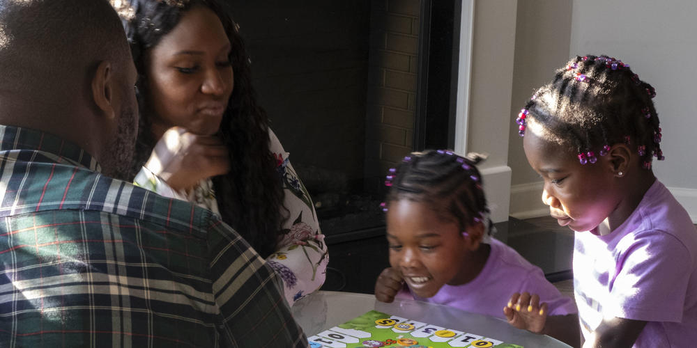 Justice Altidor, center, and her twin sister, Journey play a game with their mom and dad.