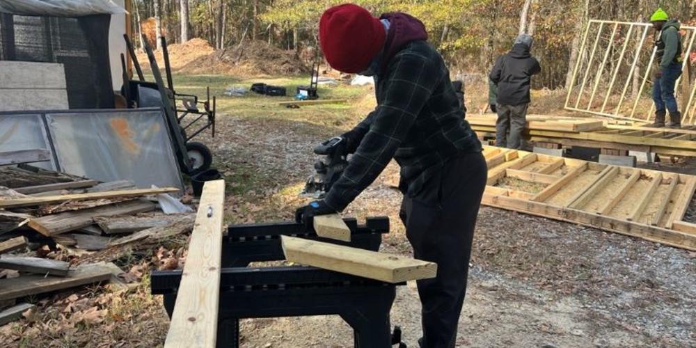 G2G Student Bridget Darby saws wood supports for a shed building project.